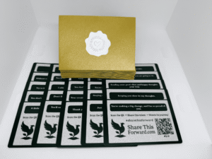 Set of 25 Share This Forward Kindness Notes paired with matching golden envelopes sealed with silver heart emblems, featuring uplifting affirmations and scannable QR codes to track acts of kindness and connection