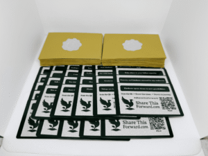 Set of 50 Share This Forward Kindness Notes featuring uplifting affirmations and unique QR codes to track their journeys, displayed with elegant golden envelopes sealed with silver heart stickers — designed to inspire meaningful acts of kindness and connection